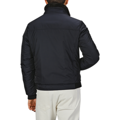 Back view of an individual wearing a Moorer Navy Blue Nylon Down Padded Blouson with a high collar and white pants, standing against a plain background.