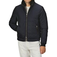 A man wearing the Moorer Navy Blue Nylon Down Padded Blouson with a zippered front and white pants. The jacket, resembling fine Italian outerwear, has a high collar and zippered pockets. The man's head is not visible.