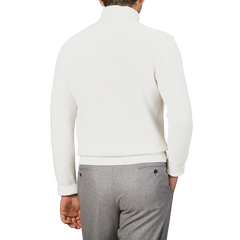 A man in a cream heavy wool cashmere rollneck by Morgano and gray pants is shown from the back against a subtle light gray background.