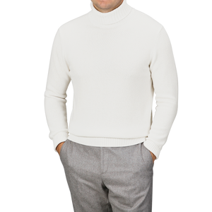 A person wearing a Cream Heavy Wool Cashmere Rollneck by Morgano and gray pants stands with hands in pockets against a plain background.