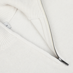 Close-up of a cream wool cashmere quarter zip from Morgano, with a partially opened zipper revealing a small white tag on the inside.