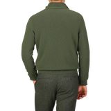 Rear view of a person wearing the Morgano Moss Green Wool Cashmere Quarter Zip and gray pants. The high-collared Italian knitwear drapes elegantly, with the person's hand resting by their side.