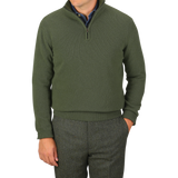 A man wearing the Moss Green Wool Cashmere Quarter Zip by Morgano, crafted from luxurious Italian knitwear, stands with one hand in his pocket against a plain gray background.