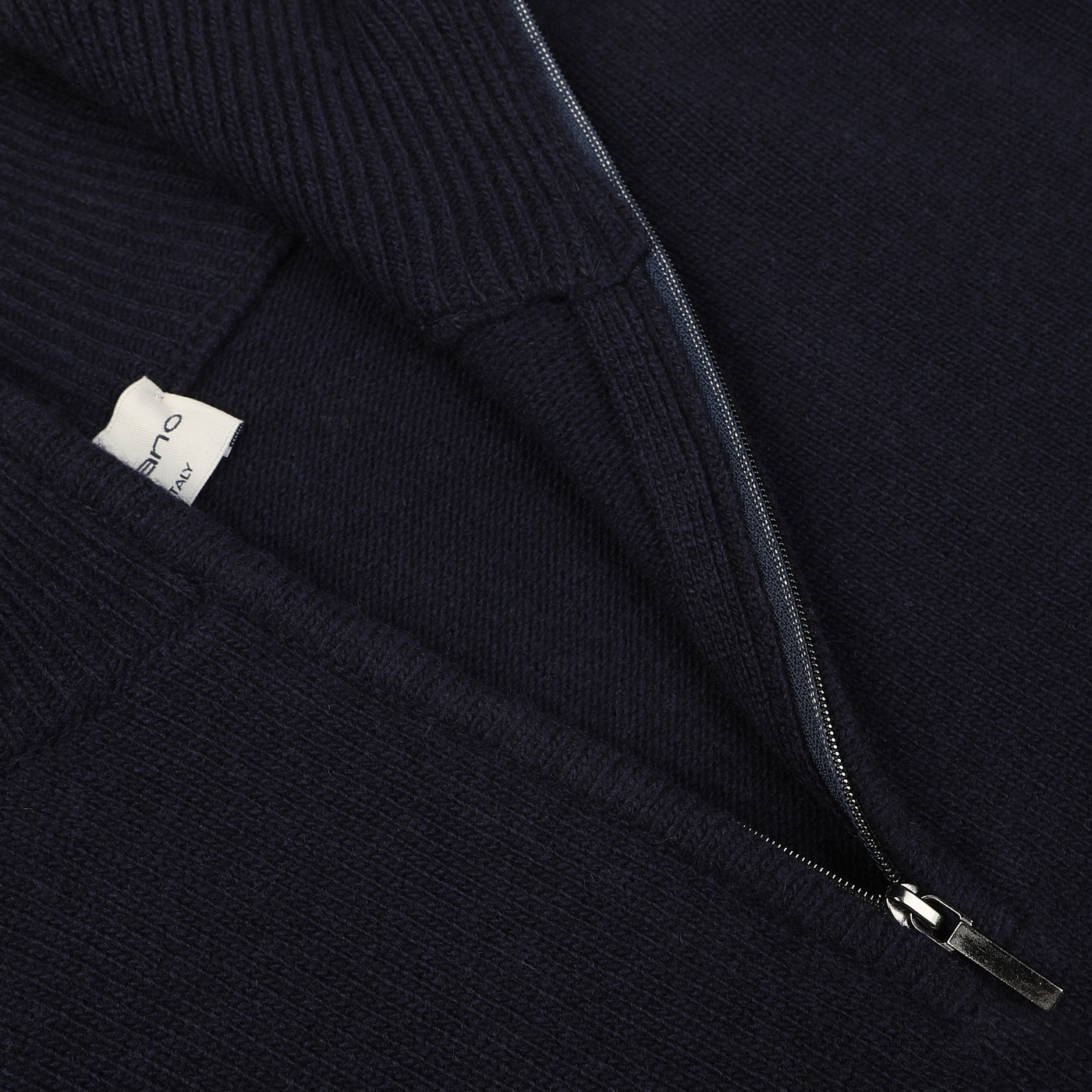 Close-up of the Morgano Navy Blue Wool Cashmere Quarter Zip sweater with a partially unzipped metal zipper, revealing a white clothing label inside. Crafted by an Italian knitwear specialist, this luxurious piece is made from the finest blend of merino wool and cashmere.