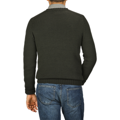 A person is standing with their back to the camera, wearing a Khaki Green Merino Wool Garbis Sweater by Nitto and blue jeans.