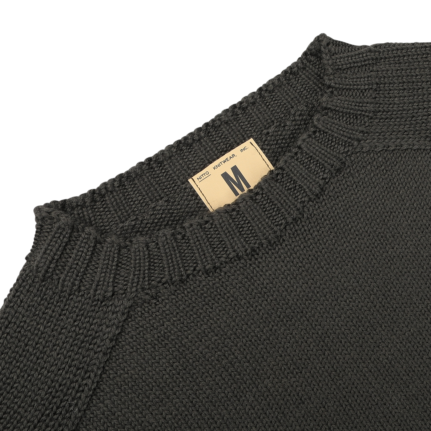 Close-up of a khaki green Merino Wool Garbis sweater from Nitto with a beige size tag labeled "M" near the collar.