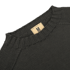 Close-up of a khaki green Merino Wool Garbis sweater from Nitto with a beige size tag labeled "M" near the collar.