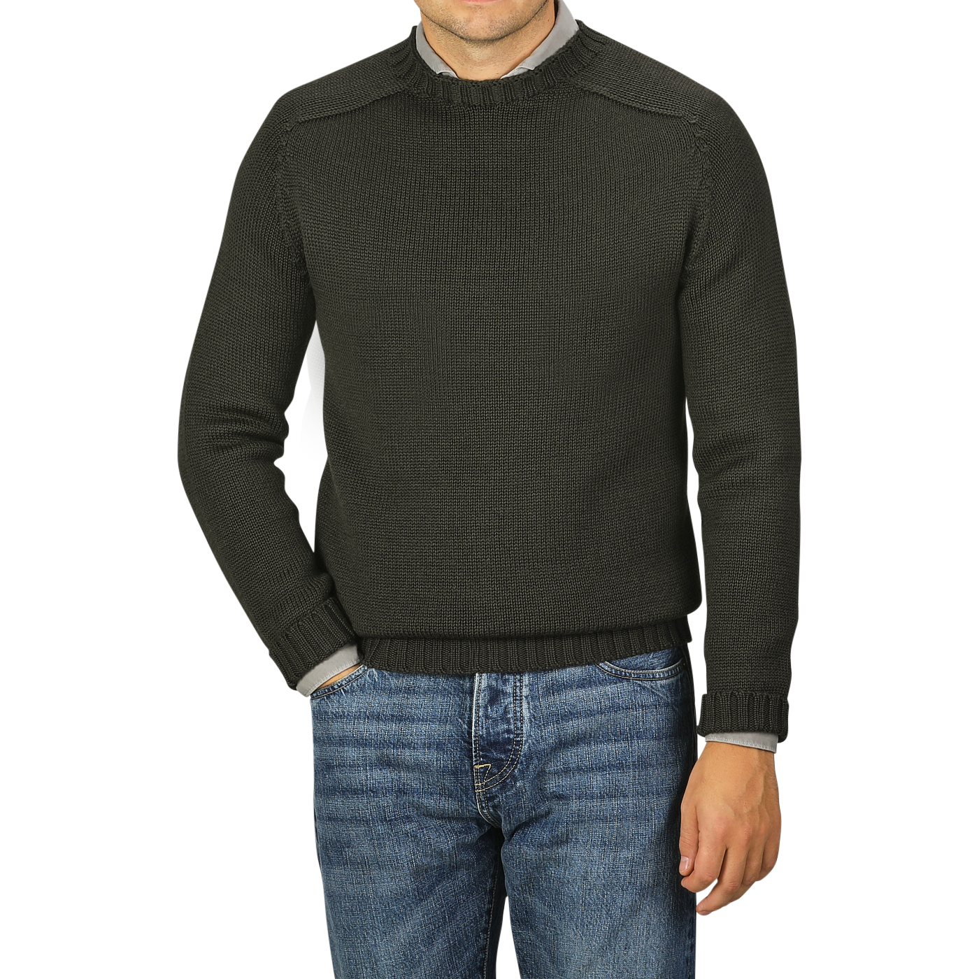 A man wearing a Nitto Khaki Green Merino Wool Garbis Sweater and blue jeans stands against a plain grey background, with only his torso and part of his arms visible.