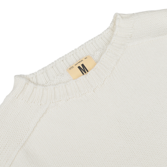 A close-up of an Ecru White Merino Wool Garbis Sweater from Nitto features a ribbed neckline and a size label marked "Medium.