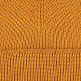 Close-up of an Ocre Yellow Merino Wool Ara Beanie by Nitto, highlighting its ribbed texture and stitching details, crafted by a knitwear specialist.