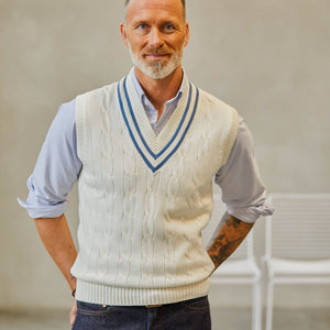 A man with a beard wearing an Alan Paine Off-White Blue Striped Cotton Cricket Slipover over a striped shirt, standing with his hands on his hips.