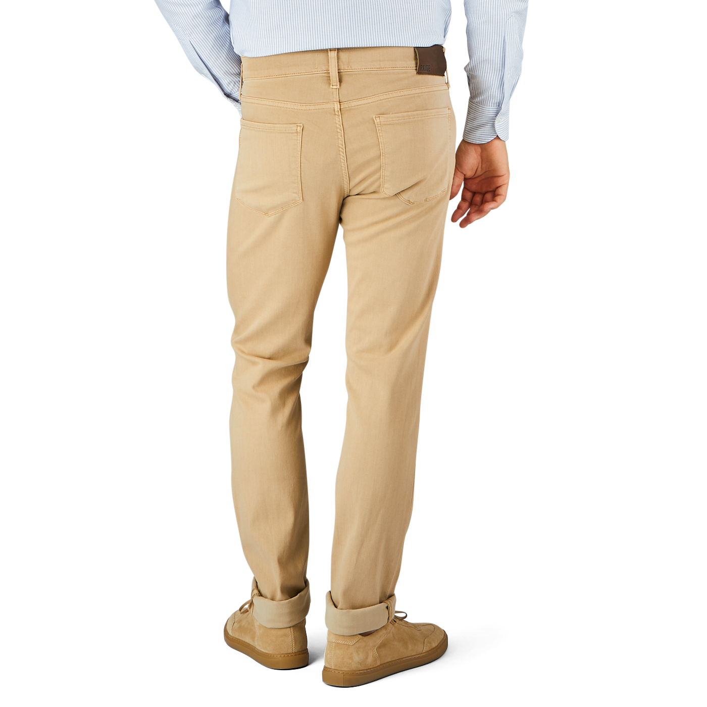 A person wearing beige pants with a comfortable fit and a light blue shirt is shown from the back. The Caramel Beige Cotton Transcend Federal Slim Jeans, possibly by Paige, have two back pockets. They are also wearing brown shoes.