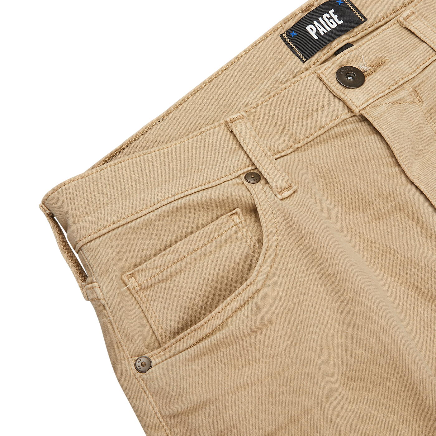 Close-up of beige pants with a visible label reading "PAIGE" above the waistband, showcasing belt loops, front pocket, and button closure on a light surface. These Caramel Beige Cotton Transcend Federal Slim Jeans are crafted from Transcend fabric for a comfortable fit.