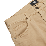 Close-up of beige pants with a visible label reading "PAIGE" above the waistband, showcasing belt loops, front pocket, and button closure on a light surface. These Caramel Beige Cotton Transcend Federal Slim Jeans are crafted from Transcend fabric for a comfortable fit.
