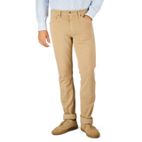 A person wearing a light blue shirt, Caramel Beige Cotton Transcend Federal Slim Jeans from Paige rolled up slightly at the bottom for a comfortable fit, and beige shoes stands against a plain background.