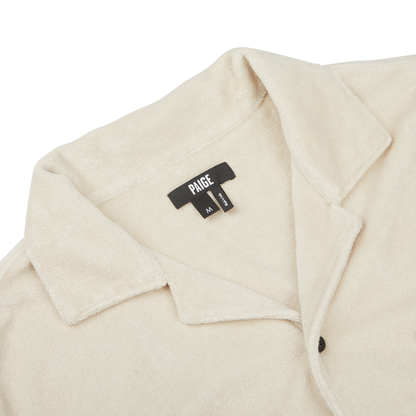Close-up of a Cream Beige Cotton Towelling Polo Shirt with a front button opening, collared design, and a black fabric tag displaying the brand "Paige" and size "M".