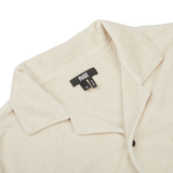 Close-up of a Cream Beige Cotton Towelling Polo Shirt with a front button opening, collared design, and a black fabric tag displaying the brand "Paige" and size "M".
