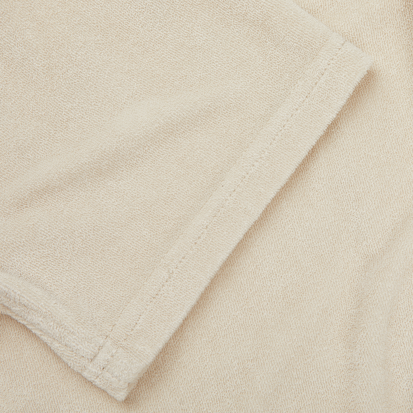 Close-up of the folded edge of a beige towel, displaying its texture and stitching, reminiscent of the soft finish found on a Paige Cream Beige Cotton Towelling Polo Shirt.