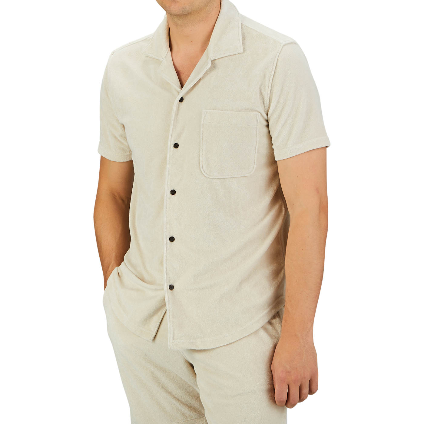 A person wearing a Cream Beige Cotton Towelling Polo Shirt by Paige with a front pocket and matching pants stands against a plain gray background.