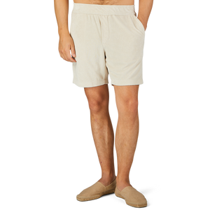 A person wearing Paige's Cream Beige Cotton Towelling Shorts with a drawstring waist and beige slip-on shoes is standing against a plain background with one hand in their pocket.