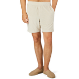 A person wearing Paige's Cream Beige Cotton Towelling Shorts with a drawstring waist and beige slip-on shoes is standing against a plain background with one hand in their pocket.
