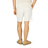 The back view of a man wearing Ecru Cotton Blend Philips Shorts by Paige and a tan shirt.