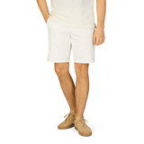 A man wearing white stretch shorts, the Ecru Cotton Blend Philips Shorts by Paige, and a tee shirt.
