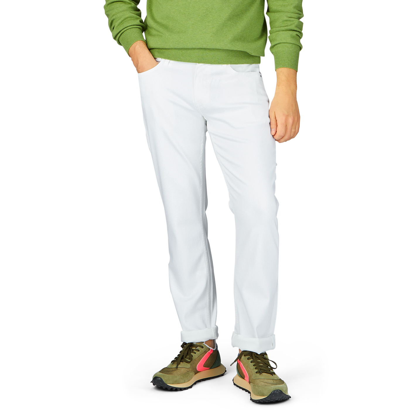 Man in green sweater and Paige Icecap White Cotton Transcend Federal Slim Jeans standing with one hand in pocket, wearing multicolored sneakers.