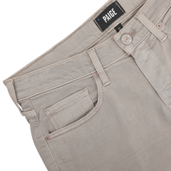 The Moroccan Clay Cotton Transcend Federal Slim Jeans, crafted by Paige, showcase a unique Moroccan clay color and feature light beige denim. The jeans include a front pocket with a visible button and the "Paige" label elegantly displayed on the waistband, enhancing their versatile style.