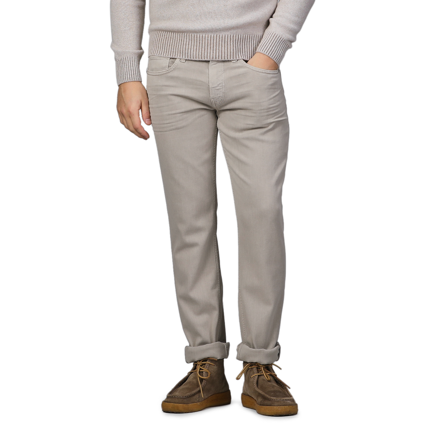 A person poses against a gray background, wearing a beige sweater, Paige Moroccan Clay Cotton Transcend Federal Slim Jeans, and brown shoes.