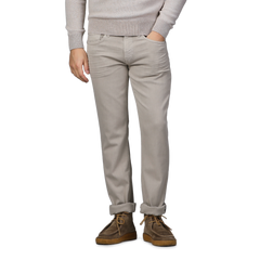 A person poses against a gray background, wearing a beige sweater, Paige Moroccan Clay Cotton Transcend Federal Slim Jeans, and brown shoes.