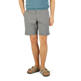 Man in a blue t-shirt and Slate Grey Cotton Blend Phillips shorts by Paige, wearing beige sandals, standing on a yellow textured surface.