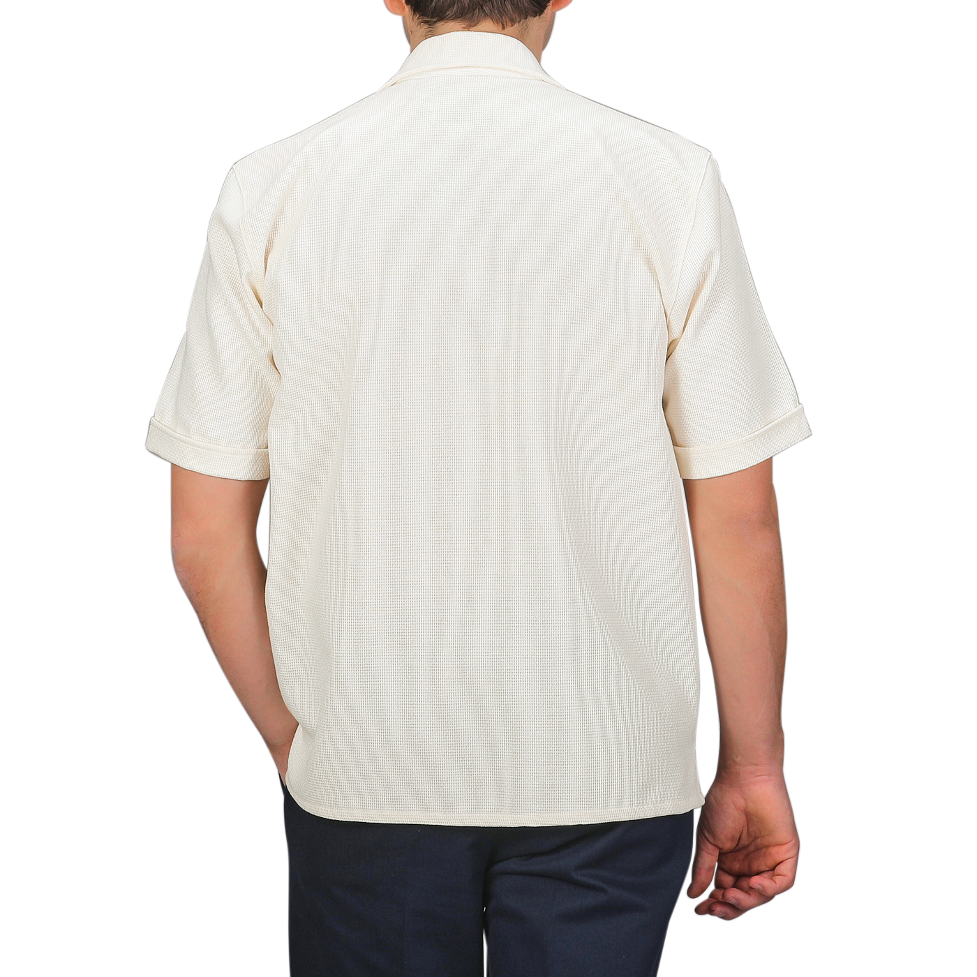 A person wearing a Peregrine Cream Dry Cotton Cuban Collar Shirt with dark pants stands back to the camera against a gray background, highlighting the pure cotton fabric.