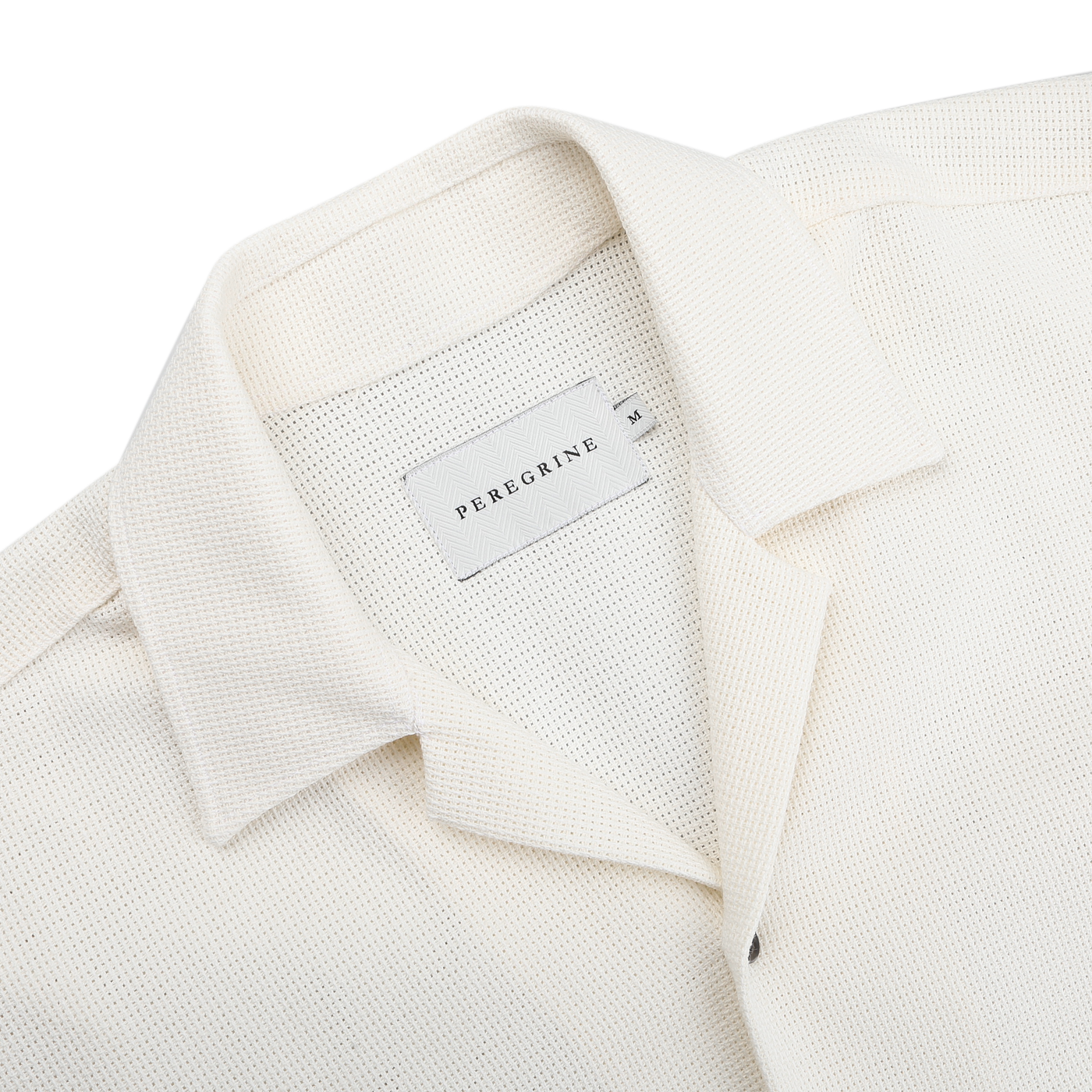 Close-up of the Cream Dry Cotton Cuban Collar Shirt by Peregrine, featuring a Cuban collar and crafted from pure cotton with a label on the inner neck.