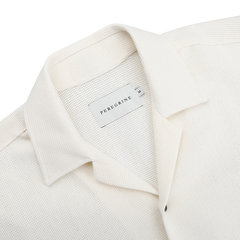 Close-up of the Cream Dry Cotton Cuban Collar Shirt by Peregrine, featuring a Cuban collar and crafted from pure cotton with a label on the inner neck.