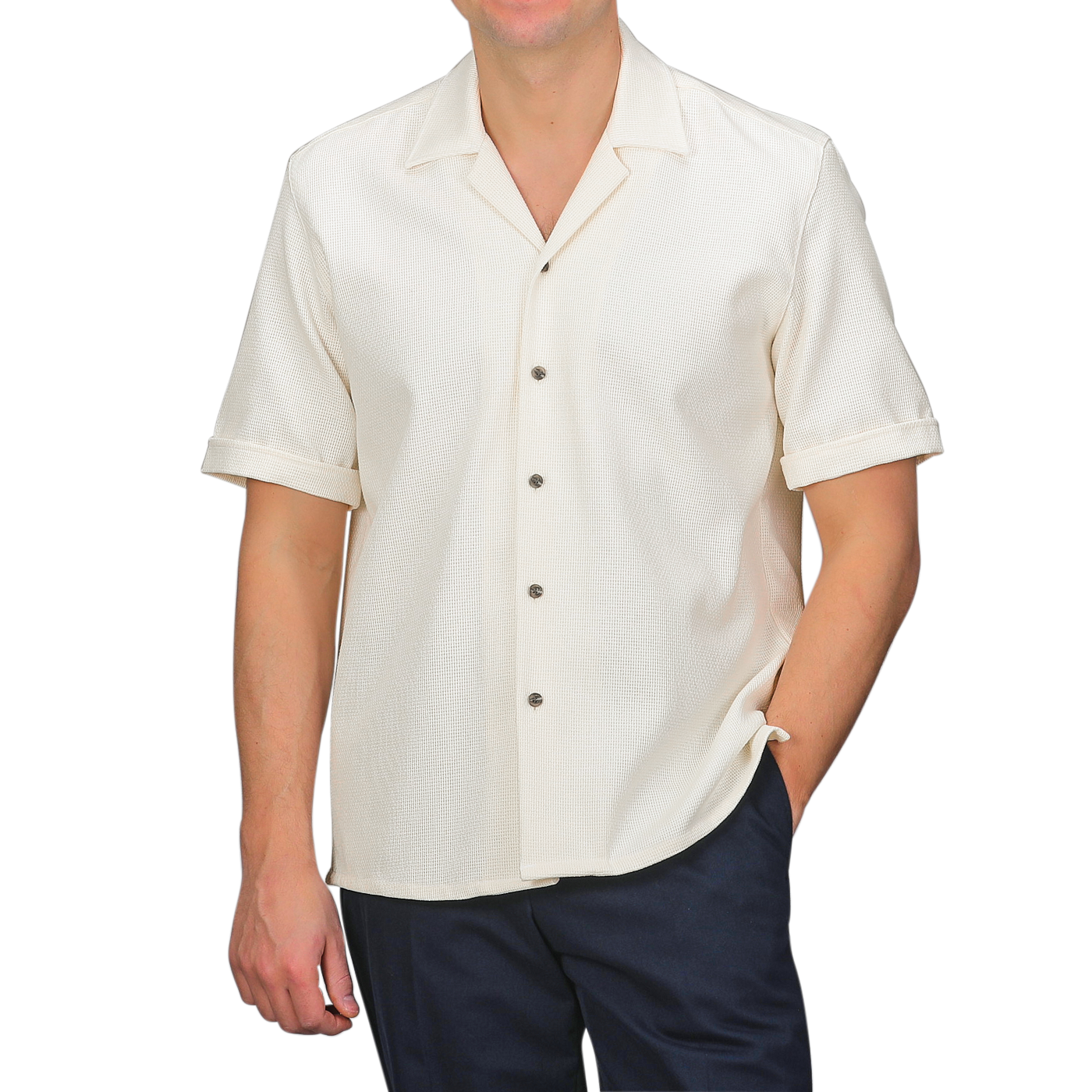 An individual stands against a gray backdrop, wearing Peregrine's Cream Dry Cotton Cuban Collar Shirt paired with dark pants.