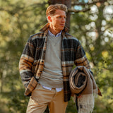 A man in a Peregrine Grey Barney Checked Wool Tweed Overshirt and tan pants is holding a scarf.
