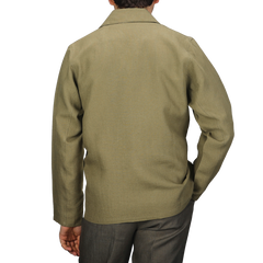 Wearing a Khaki Green Linen Grange Shacket by Peregrine, a person stands against a gray backdrop, showcasing understated style from behind.