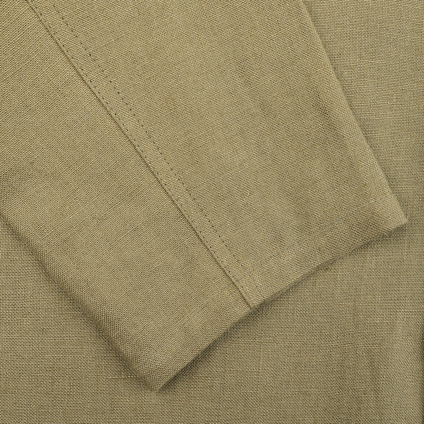 Close-up of a folded khaki green fabric from the Peregrine Khaki Green Linen Grange Shacket, highlighting a seam with visible stitching detail.