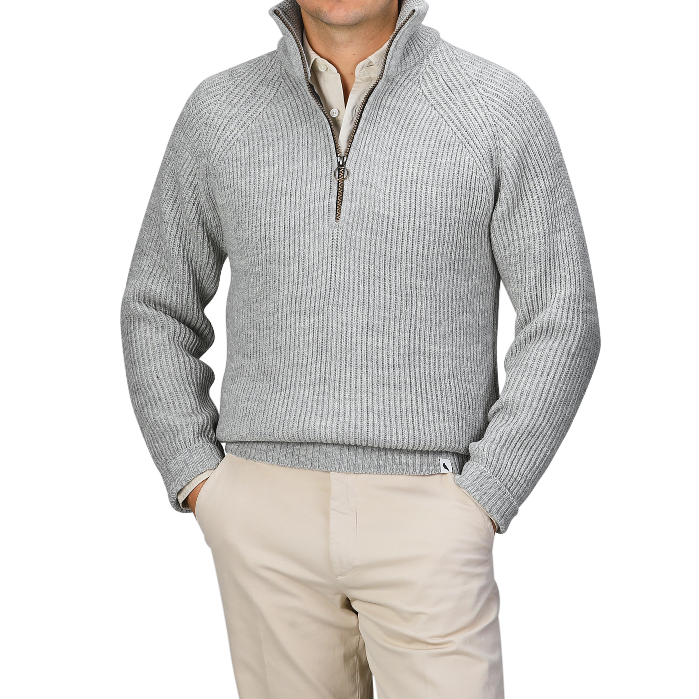 A person is elegantly dressed in a light grey wool Ford Zip Neck Sweater by Peregrine, layered over a white collared shirt and paired with beige pants.