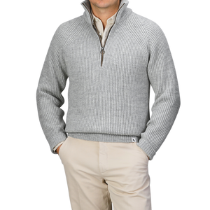 A person is elegantly dressed in a light grey wool Ford Zip Neck Sweater by Peregrine, layered over a white collared shirt and paired with beige pants.