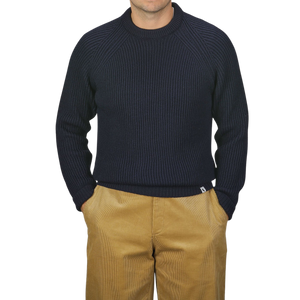 A person wearing a Peregrine Navy Blue Wool Ford Raglan Crewneck sweater and tan pants stands against a neutral background with their hands in their pockets.