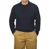 A person wearing a Peregrine Navy Blue Wool Ford Raglan Crewneck sweater and tan pants stands against a neutral background with their hands in their pockets.