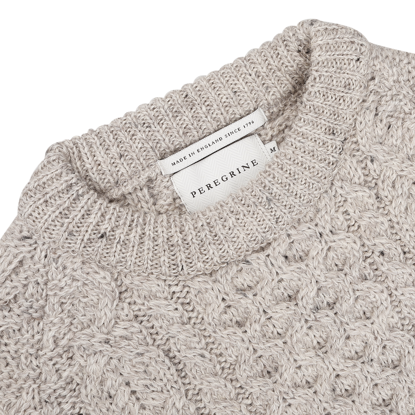 Close-up of the Skiddaw Beige Merino Wool Hudson Aran Jumper, highlighting its textured pattern and the rich heritage of British knitwear. A label reads "Peregrine, Made in England Since 1796.