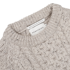 Close-up of the Skiddaw Beige Merino Wool Hudson Aran Jumper, highlighting its textured pattern and the rich heritage of British knitwear. A label reads "Peregrine, Made in England Since 1796.