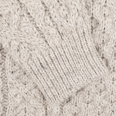 Close-up of a textured, Skiddaw Beige Merino Wool Hudson Aran Jumper by Peregrine, featuring a cable pattern and ribbed cuff that highlights the tradition of British knitwear.