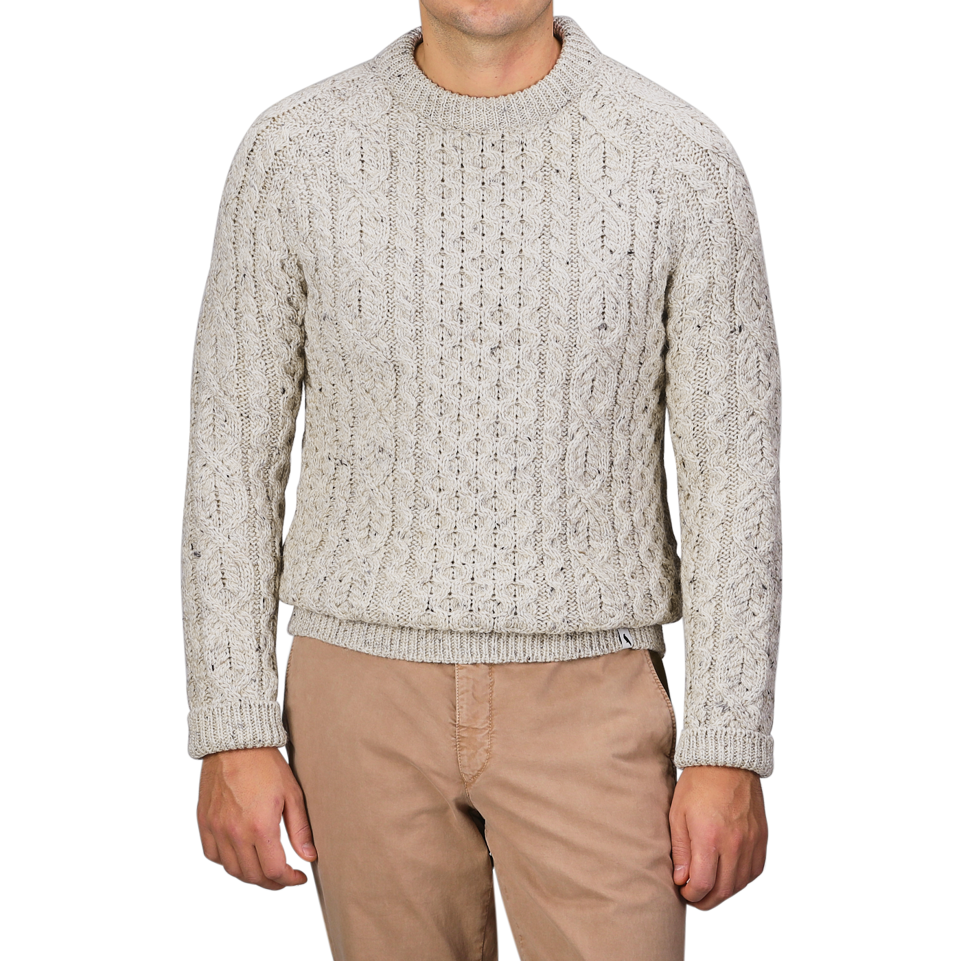 A person wearing a Peregrine Skiddaw Beige Merino Wool Hudson Aran Jumper and tan pants stands against a gray background, with their head not visible.