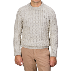 A person wearing a Peregrine Skiddaw Beige Merino Wool Hudson Aran Jumper and tan pants stands against a gray background, with their head not visible.