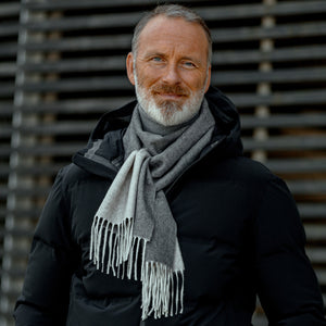 A man in a black coat wearing a Light Grey Taupe Two-Sided Silk Cashmere Scarf by Piacenza Cashmere with fringed endings.