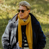 A man wearing sunglasses and a Mustard Yellow Cashmere Aeternum Scarf by Piacenza Cashmere with fringed endings.